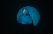 Γυναίκα που φοράει χιτζάμπ, στέκεται μπροστά από μαύρο τοίχο