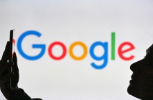 Άτομο κρατά ένα κινητό μπροστά από το λογότυπο της Google