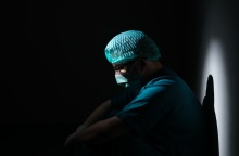 Γιατρός κουρασμένος φορά μάσκα και στέκεται στο ημίφως