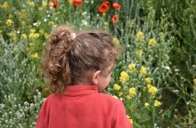 Παιδί ποζάρει γυρισμένο πλάτη έχοντας ως φόντο λουλούδια