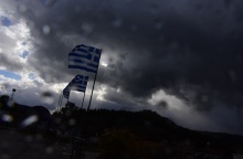 Σταγόνες βροχής πάνω σε τζάμι και στο φόντο ελληνικές σημαίες 