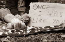 Άστεγος με τρύπια και βρώμικα ρούχα με χαρτόνι στο οποίο γράφει «Κάποτε ήμουν σαν εσένα»