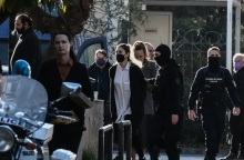 Η Ρούλα Πισπιρίγκου με λευκό πουκάμισο και μαύρο πανωφόρι οδηγείται στην ανακρίτρια