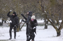 Νεαρά άτομα παίζουνε με το χιόνι, φορώντας ζεστά ρούχα