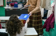 Μαθήτρια παίρνει το τετράδιο της από τη δασκάλα της σε αίθουσα δημοτικού σχολείου