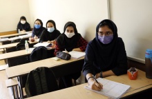 Μαθήτριες σε σχολείο στο Ιράν κάθονται στα έδρανα έχοντας ανοίξει τα τετράδια τους και φορώντας τις μάσκες τους