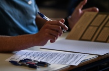 Το τετράδιο απαντήσεων για τα θέματα των Νέων Ελληνικών στα οποία εξετάστηκαν τα ΕΠΑΛ - Οι κόλλες με τα θέματα και στιλό πάνω στο θρανίο - Διακρίνεται το χέρι υποψηφίου