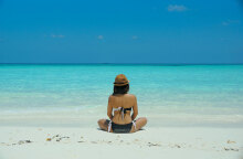 Κοπέλα με μαγιό κάθεται σε αμμώδη παραλία