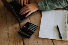 Άτομο υπολογίζει τα οικονομικά του σε κομπιουτεράκι, υπολογιστή και χαρτί