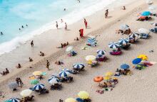 Λουόμενοι απολαμβάνουν τον ήλιο, το κολύμπι και τα παιχνίδια σε παραλία της Λευκάδας - Στημένες ομπρέλες και απλωμένες πετσέτες στην αμμουδιά