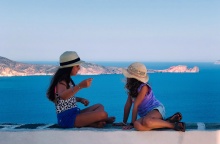 Παιδιά κάθονται σε πεζουλάκι νησιού και φωτογραφίζονται με φόντο τη θέα
