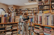 Νεαρή γυναίκα σε βιβλιοπωλείο εξετάζει προσεκτικά τα βιβλία που επιθυμεί να αγοράσει