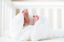 Νεογέννητο μωρό έχει σηκώσει τα ποδαράκια του τα οποία φαίνονται από το σεντόνι με το οποίο είναι καλυμμένο το βρέφος