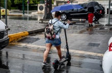 Γυναίκα με πατίνι κρατά ομπρέλα για να προστατευτεί από τη βροχή