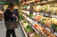 Γυναίκα με το καλάθι ανά χείρας στο ψυγείο με τα λαχανικά σε σούπερ μάρκετ επιλέγει προϊόντα