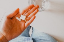 Γυναίκα κρατά στη χούφτα της χάπια και δίπλα της έχει ένα ποτήρι νερό