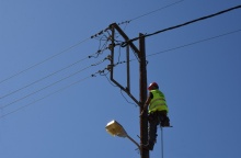 Άνδρας πραγματοποιεί εργασίες σκαρφαλωμένος σε κολώνα της ΔΕΗ - Φορά ανακλαστικό και προστατευτικό κράνος