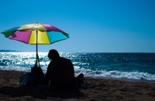 Άνδρας καθισμένος κάτω από πολύχρωμη ομπρέλα θαλάσσης στην ακροθαλασσιά