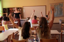 Εκπαιδευτικός σε σχολική αίθουσα με παιδιά που σηκώνουν το χέρι τους για να πουν μάθημα