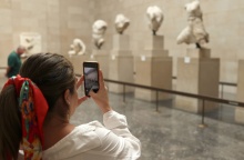 Τεκμήρια στο Βρετανικό Μουσείο και γυναίκα στα αριστερά της οθόνης που με το κινητό της τα φωτογραφίζει