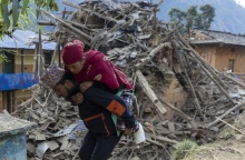 Άνδρας μεταφέρει γυναίκα στην πλάτη του ενώ πίσω τους υπάρχουν χαλάσματα από τον σεισμό στο Νεπάλ