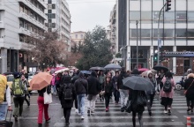 Πολίτες στο Σύνταγμα κρατούν ομπρέλα και περπατούν στον δρόμο υπό βροχή