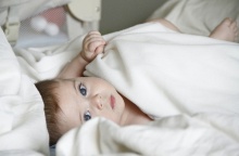 Μωρό με γαλανά μάτια κοιτά στην κάμερα ενώ είναι τυλιγμένο με σεντονάκι