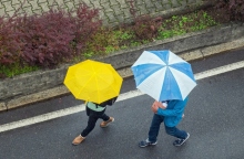 Δύο άνθρωποι περπατούν στον δρόμο κρατώντας ομπρέλα για τη βροχή