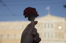 Χέρι κρατά κόκκινο τριαντάφυλλο με φόντο τη Βουλή των Ελλήνων