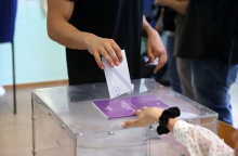 Χέρι που ρίχνει φάκελο στην κάλπη και άλλο χέρι που βγάζει το βιβλίο από τη σχισμή της κάλπης