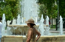 Γυναίκα με καπέλο περπατά εν μέσω καύσωνα δίπλα από το σιντριβάνι της πλατείας Συντάγματος