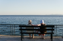 Ηλικιωμένες κυρίες κάθονται φορώντας τα καπελάκια τους σε παγκάκι με θέα τη θάλασσα