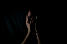 Γυναίκα που κλαίει κρατά το πρόσωπό της ενώ βρίσκεται στο ημίφως - Εικόνα που παραπέμπει σε κακοποίηση και ενδοοικογενειακή βία