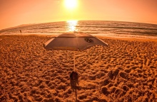 Φωτογραφία από παραλία εν μέσω καύσωνα με τον φακό να καταγράφει τον ήλιο και ομπρέλα σε παραλία