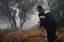 Πυροσβέστης επιχειρεί με μάνικα σε σημείο όπου η φωτιά σβήνει 