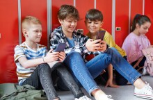 Παιδιά με κινητά καθισμένα στο πάτωμα διαδρόμου σχολείου