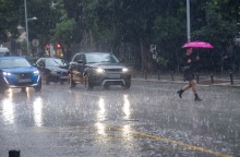 Γυναίκα με ομπρέλα διασχίζει δρόμο υπό καταρρακτώδη βροχή