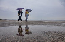 Γυναίκες περπατούν στην παραλία της Θεσσαλονίκης, κρατώντας την ομπρέλα τους