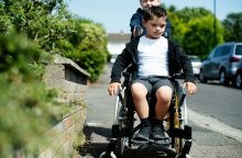 Παιδί οδηγεί το καρότσι παιδιού με κινητικές δυσκολίες