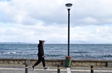 Κοπέλα περπατά με ζακέτα σε παραλιακό μέρος με πολύ αέρα