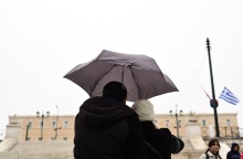 Πολίτες με ομπρέλα προστατεύονται από τη βροχή μπροστά από τη Βουλή