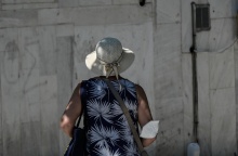 Γυναίκα με γυρισμένη πλάτη στον φακό και τη μάσκα προστασίας από τον κορωνοϊό αφημένη στον αγκώνα