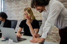 Εργαζόμενος κοιτά σε υπολογιστή πάνω από άλλη εργαζόμενη που κοιτά σε υπολογιστή