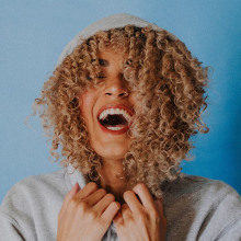 Κοπέλα με σγουρά μαλλιά φοράει κουκούλα και γελάει