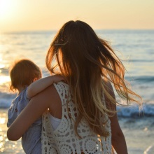 Γυναίκα με μωρό στην αγκαλιά στέκεται μπροστά σε θάλασσα