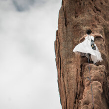 Γυναίκα με λευκό φόρεμα σκαρφαλώνει σε κάθετο βράχο
