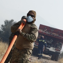 Πυροσβέστης και εθελοντής κουβαλούν τη μάνικα από το πυροσβεστικό όχημα για την κατάσβεση φωτιάς