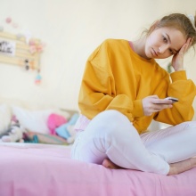 Έφηβη στεναχωρημένη στο δωμάτιο της κρατά και κοιτά κινητό