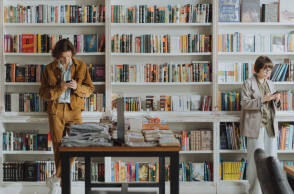 Ένας άντρας και μια γυναίκα στη βιβλιοθήκη, κοιτάνε τα κινητά τους