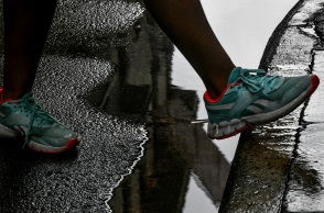 Πόδι με αθλητικό παπούτσι περνά πάω από λιμνάζοντα νερά σε δρόμο